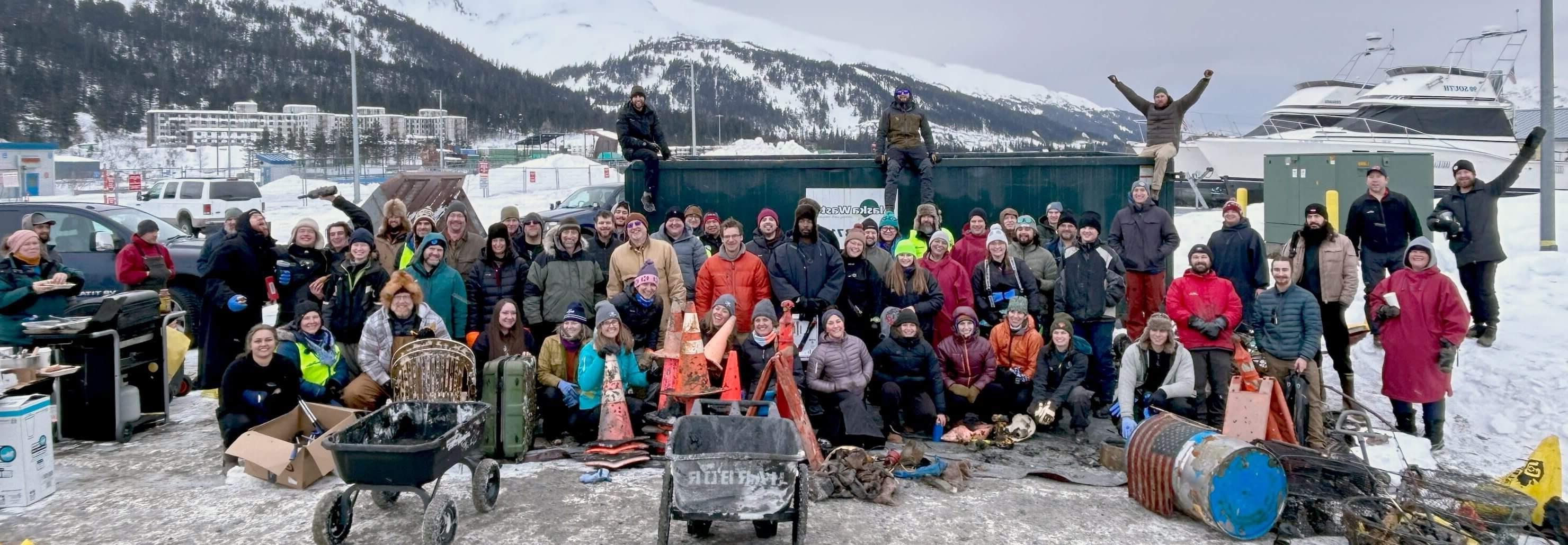 Dive Alaska volunteers bundled in warm clothes pose in a group photo with the objects they've retrieved from the water.